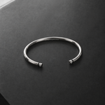 A polished silver cuff bangle bracelet with small bead details at the open ends, resting on a dark gray textured surface.