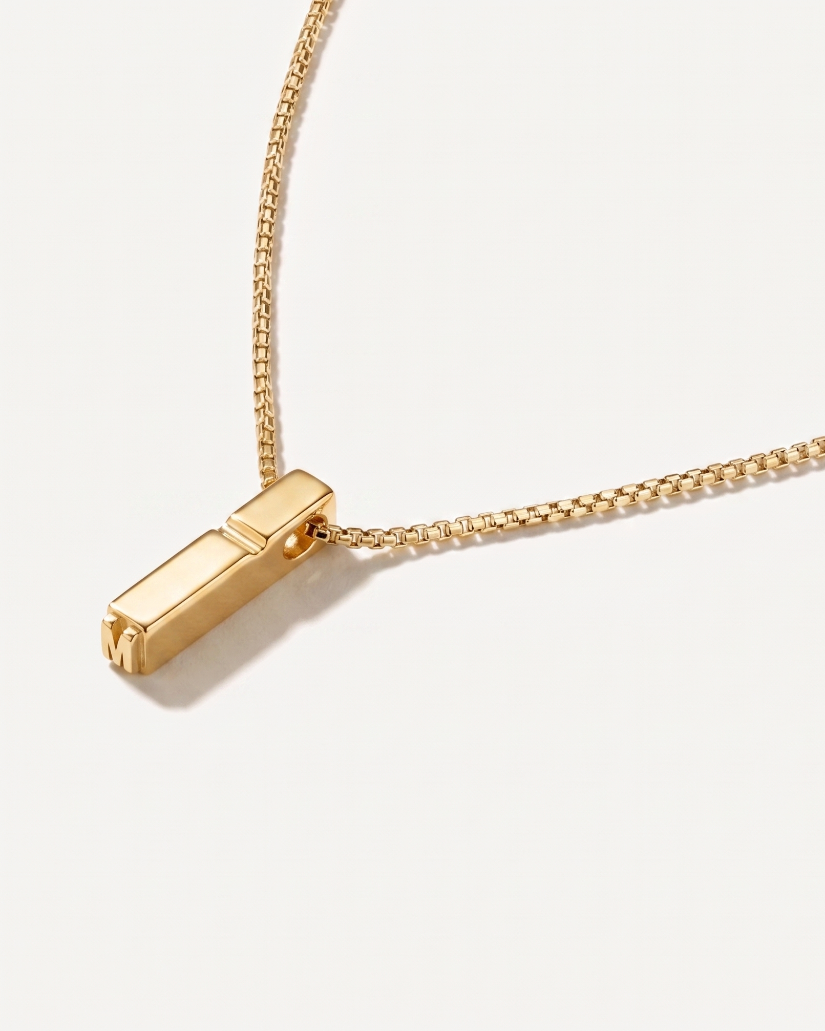 Gold necklace with a rectangular pendant on a light background