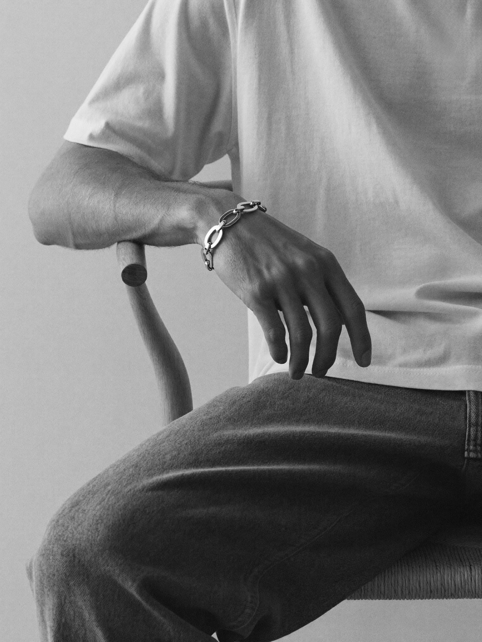 Person wearing a bracelet sitting on a chair with a plain background