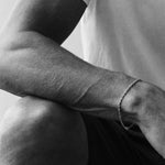 Black and white close-up of a person's arm with a bracelet, wearing a t-shirt.