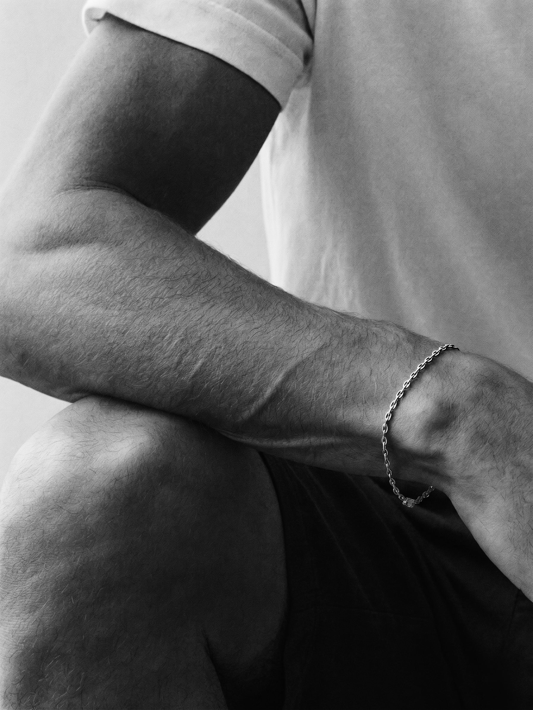 Black and white close-up of a person's arm with a bracelet, wearing a t-shirt.