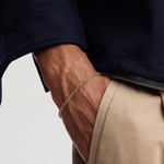 Close-up of a person wearing a gold bracelet on a plain background
