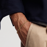 Close-up of a person wearing a gold bracelet on a plain background